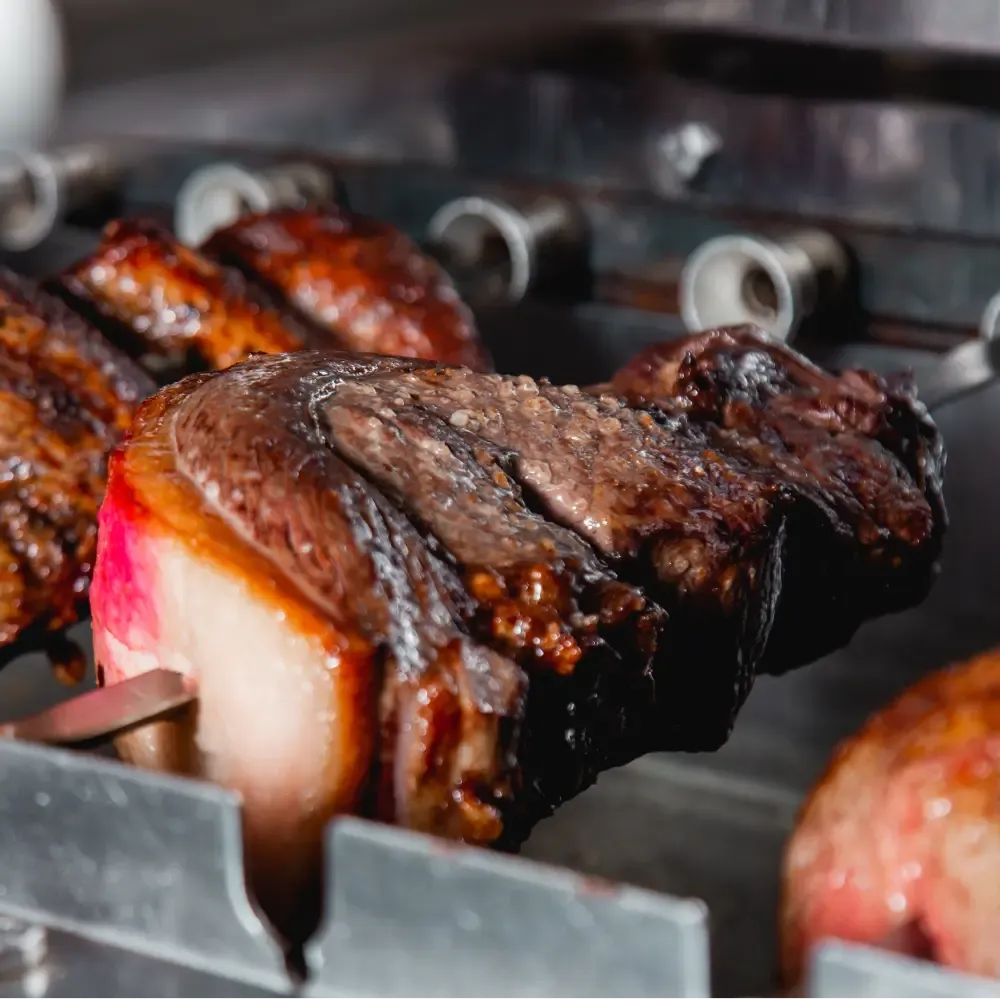 Juicy picanha beef with a thick fat cap cooking on a metal skewer in a churrascaria.